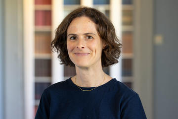 A woman, wearing a black jumper, smiles at the camera. She has dark auburn hair cut in a long bob.
