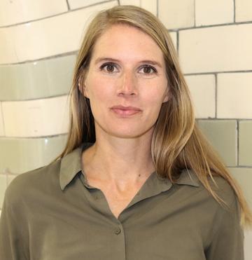 A white woman with long blonde hair smiles at the camera. She is wearing a brown shirt.
