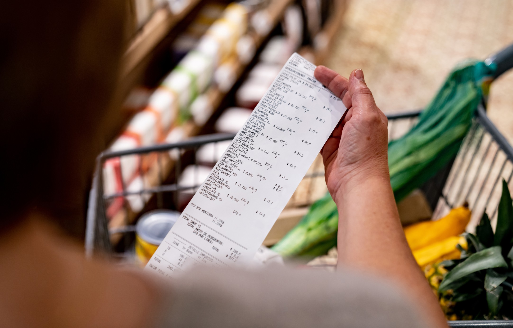 A person holds a till receipt in front of a basket of groceries.