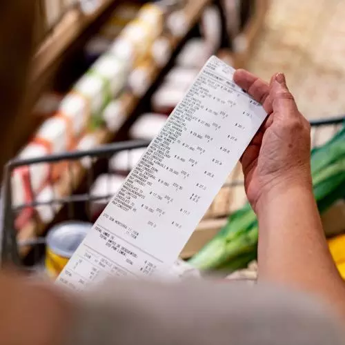 A person holds a till receipt in front of a basket of groceries.
