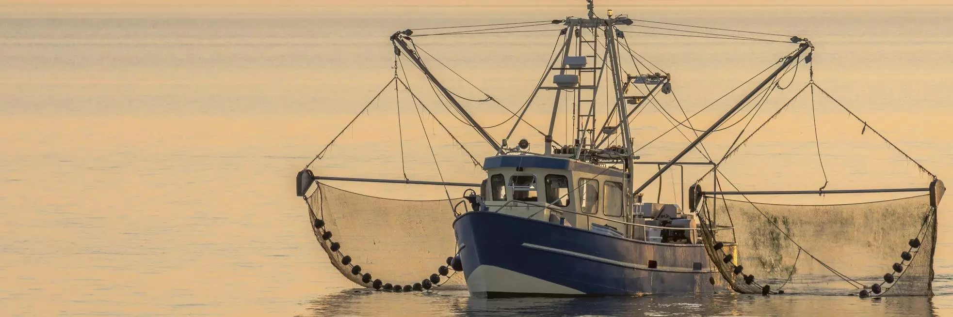A fishing boat with nets in the water rests at sea. The sky is orange.